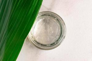 Jar with transparent cosmetic gel with leaves on marble background. Aloe vera cream-gel. Copy space photo