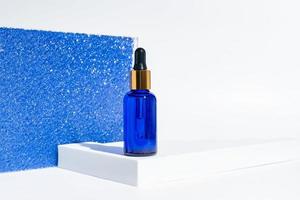 blue glass bottle with beauty serum, hyaluronic acid, collagen and vitamins on a sparkling blue background. Luxury home face and body care treatment concept. Copy space photo