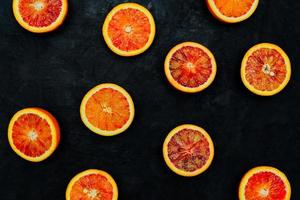 Blood Oranges. Halved blood oranges scattered on a black stone background. Top view, blank space. photo