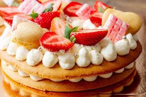 Sponge cake with strawberries, pink milk chocolate bars, silver sprinkles, vanilla cream and heart chape cookies close up. Summer sweet dessert for birthday or mothers day photo