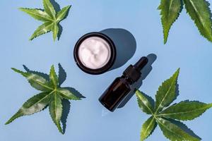 Cannabis face cream or serum or oil dropper concept. Natural cosmetic. CBD oil, THC tincture and hemp leaves on a blue background photo