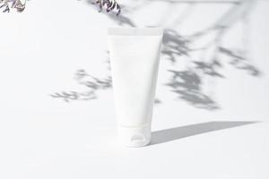 white cosmetic tube for face or body cream, cleanser or shampoo on a white background with leaves shadows. Concept of minimalism in cosmetic packaging. Copy space. photo