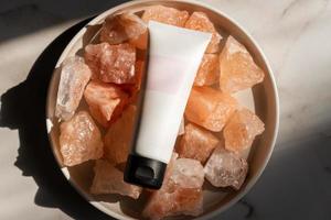 Unbranded tube with body care cosmetics lies on crystals of pink himalayan salt. Spa and wellnes concept photo