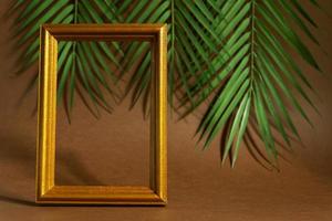 Vintage golden photoframe with neon purple feather on tropical leaves background. Trendy concept, levitation. photo