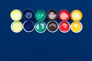 Top view of open acrylic paint cans. Colorful paints on blue background with copy space photo