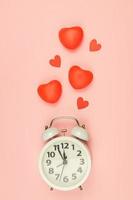 Pink Background with white alarm clock and red hearts. Creative layout. Top view. Time for love and greetings. photo