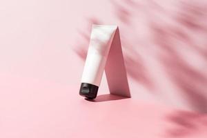 white cosmetic tube for face or body cream, cleanser or shampoo on a pink background with leaves shadows. Concept of minimalism in cosmetic packaging. Copy space photo