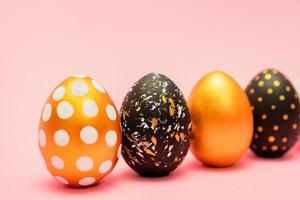Side view of pink, white, black and golden decorated easter eggs in a row on pink background. Trendy holiday backdrop. photo