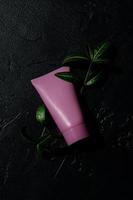 pink cosmetic tube with face or hand cream, body lotion or cleanser on a black background with deep shadows. Copy space photo