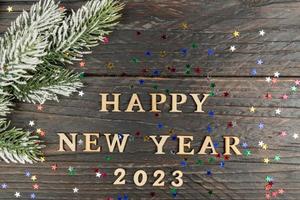 New Year's concept. Happy new year 2023 wooden text on a wooden background, fur-tree branch on the edge of the frame. photo