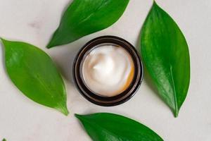 Natural moisturising cream gel in dark glass jar on green leaves as beauty flatlay, spa cosmetics and skincare closeup photo