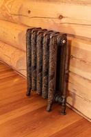 Forged Radiator in retro style in wooden logs room, room interior, wooden floor and wall, Central heating installation, warm home. photo