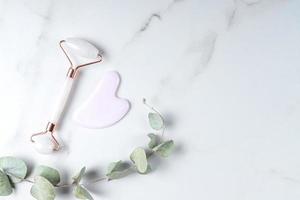 Gua Sha massager and rose quartz massage roller on marble background. Pink jade stone for face and body care. Horizontal shoot. Flat lay, top view. Copy space for your text. photo