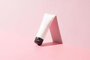 Empty white cosmetic tube for face cream, body lotion, facial cleancer or shampoo on a bright pink background with sunlight and shadows. Skin care cosmetics mockup photo