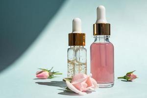 Transparent glass cosmetic bottles with a dropper on a blue background. Natural cosmetics concept, natural essential rose oil and skin care products photo