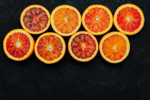 Beautiful background made of blood orange slices on black stone surface. photo