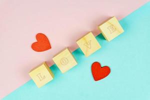 Red hearts and wooden cubes on pink and blue background. Creative flat lay with copy space. Festive greeting card for St Valentines day. Mockup photo