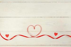 Creative Valentine Day romantic composition with red hearts, satin ribbon on wooden background. Mockup with copy space for blogs and social media. photo