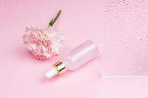 Pink transparent dropper bottle with pink beauty face oil on pink background with Carnation flower. anti aging serum with natural engredients. photo