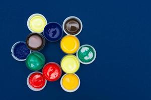 Top view of open acrylic paint cans. Colorful paints on blue background with copy space photo