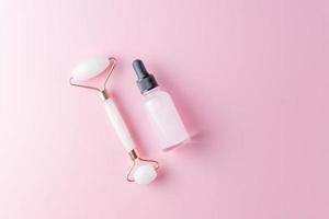 Skin care concept. Bottle of cometic product, serum or oil. Quartz roller. Cosmetics and tools on pink background photo