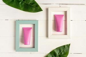 Set of cosmetics for skin care face, body or hands. Pink blank cosmetic tubes in bright frames on wooden background. Creative Cosmetic Beauty Concept. Mockup Top view. photo