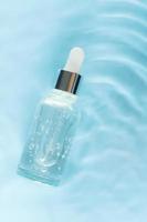 Bottle serum, oil cosmetic in clean transparent water with sunlight on blue background, flat lay, top view, copy space photo