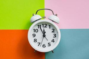 white alarm clock on abstract multicolored paper background. Minimal flat lay photo