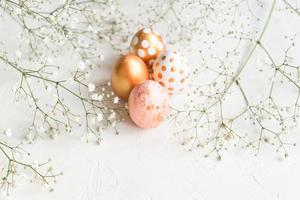 Colorful easter eggs painted in gold, white and pink colors on white background decorated with gypsophila flowers. Tender creative holiday background with copy space photo