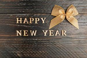 happy new year wooden text and golden bow on a wooden backgeound. Festive greeting card with copy space photo