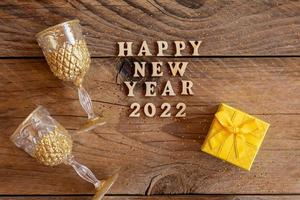 New year presents and champagne glasses on wooden table. Text Happy new year 2022. Festive greeting card. Flat lay. photo