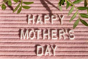 Pink letterboard with quote Happy Mother's Day, decorated with green leaves on pink background. photo