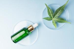 Glass bottle with cbd oil on blue background with marijuana leaf. Hemp based cosmetics. Natural herbal hemp essential oil in a glass pipette bottle photo