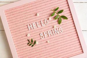 texto hola primavera en el tablero de letras rosa con ramas verdes y flores de gypsophila sobre fondo de madera, composición de estilo minimalista, espacio de copia para su texto. foto