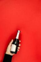 Female hand holding small champagne bottle on red, background. Mockup with copy space. photo