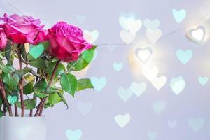 Blooming pink roses on electric hearts garland. Festive background for St valentines day. Greeting card with bokeh photo