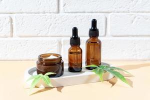 suero de aceite de cáñamo cbd en frasco cuentagotas de vidrio con hojas de cannabis, crema hidratante, suero, loción, aceite esencial. hojas de cannabis con productos cosméticos para el cuidado de la piel. cosmética natural ecológica foto