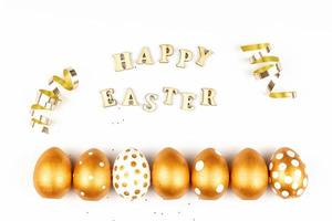 Easter festive decoration. Top view of easter eggs colored with golden paint and inscription in English Happy Easter. Wooden letters on white background. Various dotted design photo