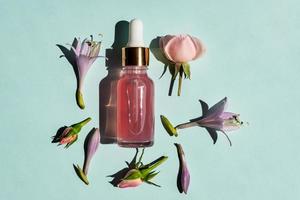 Transparent glass cosmetic bottle with a dropper on a blue background. Natural cosmetics concept, natural essential rose oil and skin care products photo