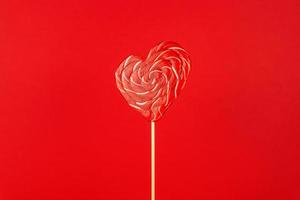 Single Valentines Day heart-shaped lollipop on red background. photo