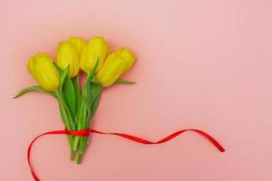 Bunch of yellow tulips with red ribbon on pink background. Festive layout. Copy space for text. Greeting card for holidays photo