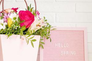 Hello Spring - text on pink felt letter board with blooming flowers and green leaves on whitebrick wall background. Springtime concept. Interior design photo