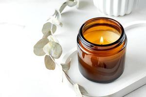 Brown burning candle on woolen table and eucalyptus branch at home in cozy atmosphere photo