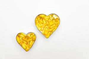 Fish oil capsules in a heart shape boxes on white background, vitamin D supplement, health care concept, top view photo