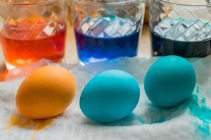 Easter Egg Dying Process. Transparent glass cups with colored water. Colored eggs in the foreground photo