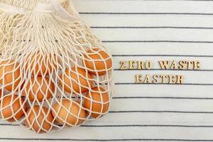 Zero waste Easter concept. No plastic bag concept. Minimal style. Beige mesh shopping bag with brown chicken eggs on textile background. photo