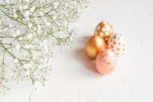 primer plano de huevos de pascua decorados en rosa, blanco y dorado con gypsophila sobre fondo de hormigón blanco. copiar espacio para texto foto