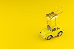Yellow retro car with golden gift box on a roof on yellow background. Festive concept of greeting christmas or birthday. photo