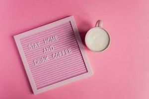 Top view of Pink Coffee cup with cappuccino and qoute Stay home and drink coffee. Self isolation and quarantine campaign to protect yourself from pandemia photo