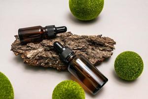 concepto de cosmética natural para el cuidado de la piel. aceite esencial o suero de vidrio oscuro en una corteza de árbol con bolas verdes. concepto ecológico natural para la marca de cosméticos. foto